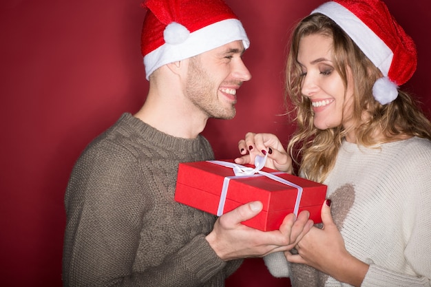 一年で最高の時期。赤で幸せに笑って一緒にプレゼントを開く若い愛情のあるクリスマスのカップルのスタジオポートレート