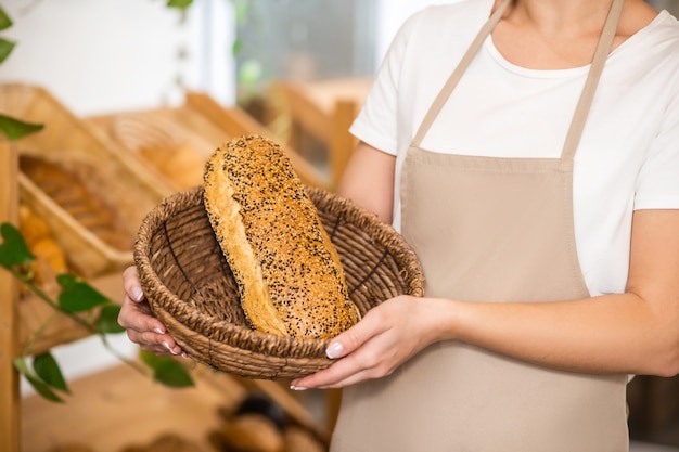 Best tradition. Neat graceful female hands carefully holding basket with freshly baked beautiful loaf of bread