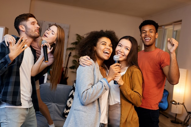 Beste karaoke-feestgroep van jonge gelukkige multiculturele vrienden die samen met microfoon zingen