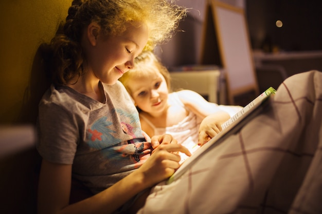 Beste vrienden van meisjes lezen sprookje voor het slapen gaan. Beste boeken voor kinderen. Zusters lezen boek in bed. Familie traditie.