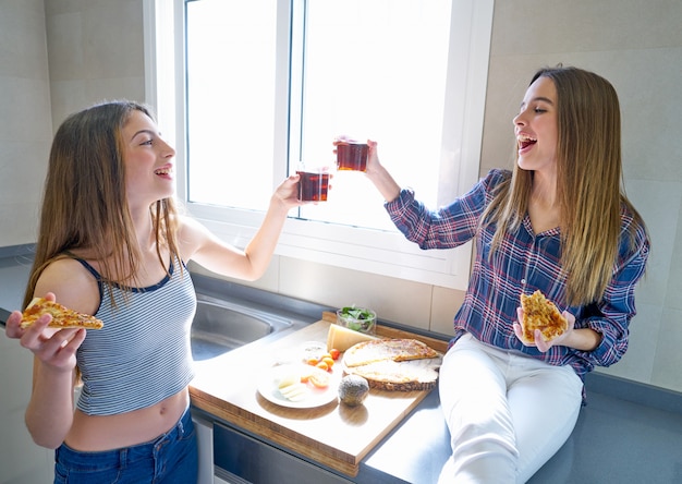 Foto beste vriendenmeisjes die pizza in de keuken eten
