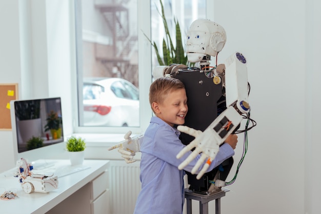 Beste vriendin. blije gelukkige jongen die terwijl het koesteren van een robot glimlacht