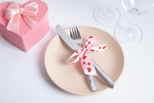 Bestek en bord met roze hartvormige geschenkdoos op de witte tafel. Serveren voor een romantisch diner op Valentijnsdag concept.