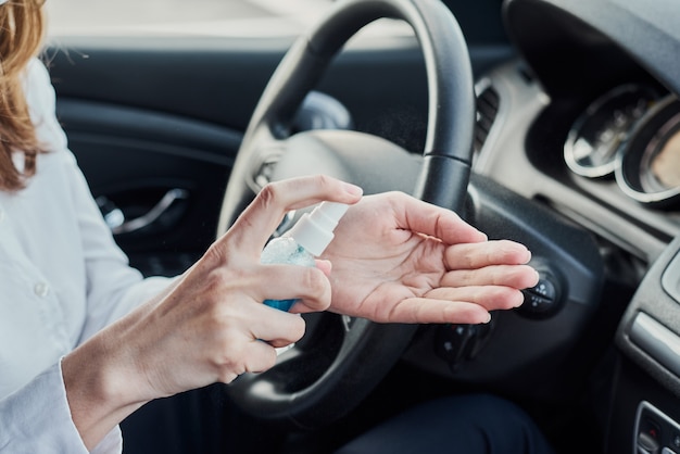Bestuurder desinfectiehanden met antibacteriële spray in de auto voor het rijden