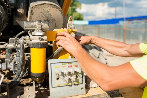 Bestuurder monteur verandert olie in een compactor op een bouwplaats, close-up