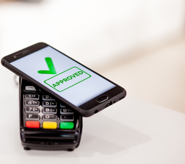 Betaalautomaat, betaalmachine met mobiele telefoon op winkelachtergrond. Contactloos betalen met NFC-technologie.