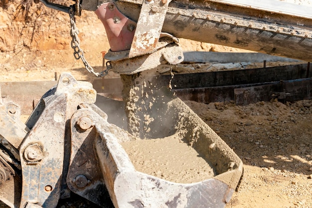 Betonmixer die vers nat beton giet in de emmer van een graafmachine op een bouwplaats