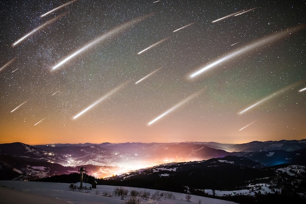 Betoverend landschap van vallende sterren op de achtergrond van de sterrenhemel op het glanzende dorp bevinden zich tussen hoge bergketens op een ijzige winternacht. Concept mystiek van UFO en abnormaal fenomeen