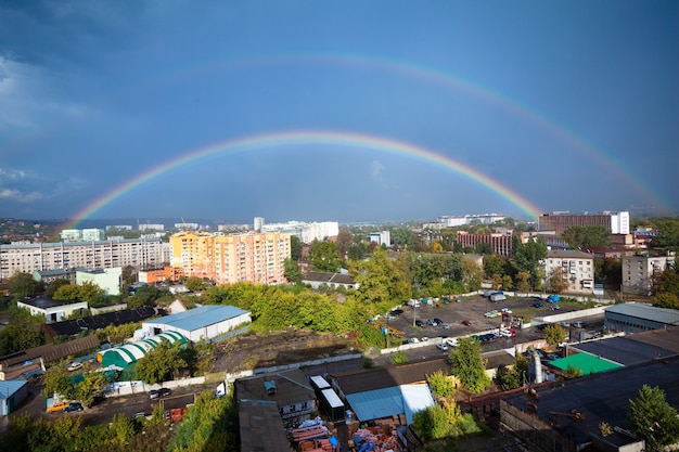 Betoverend panorama van een Europese stad met een grote mooie regenboog tegen een achtergrond van blauwe wolken en zonnestralen. Concept van een natuurlijk fenomeen. Advertentie ruimte