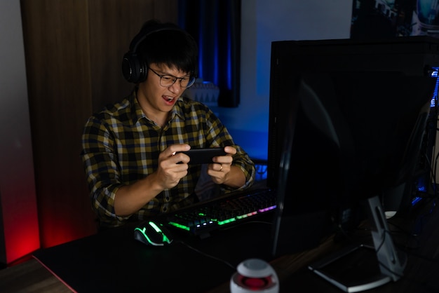 Betrokken aziatische man cyber sport gamer geconcentreerd het spelen van videogames op computer bij nacht donkere kamer thuis, esport en technologie concept.