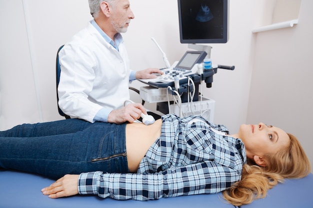 Betrokken professionele bekwame medicus die in de kliniek werkt terwijl ze ultrasone lichaamsscans uitvoeren en ultrasone apparatuur gebruiken