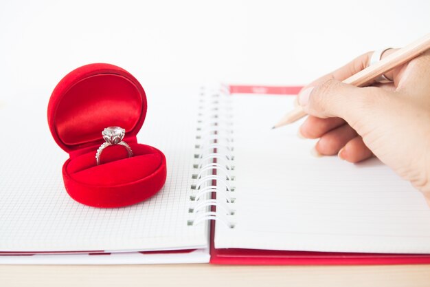 Betrokkenheid of Trouwring in rode doos met de hand die van de vrouw op notitieboekje, Liefde en de Dag van de Valentijnskaart schrijven