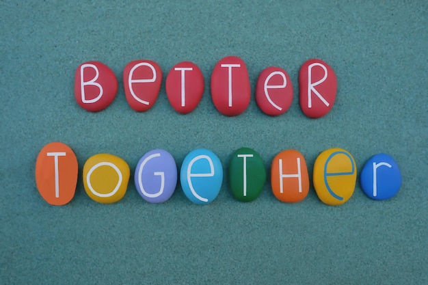 Photo better together creative slogan composed with multi colored stone letters over green sand