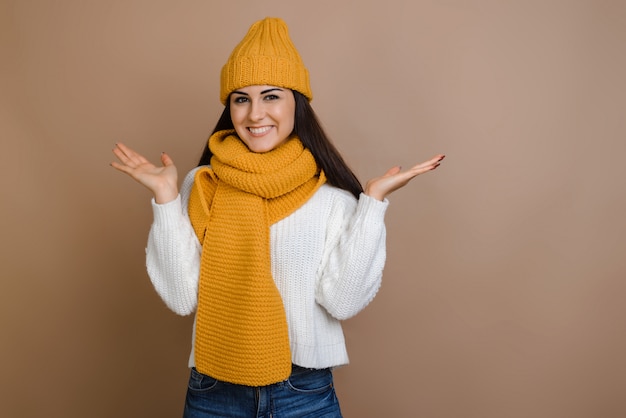 Beutiful brunette in warm hat and mittens on brown background spreading arms out.