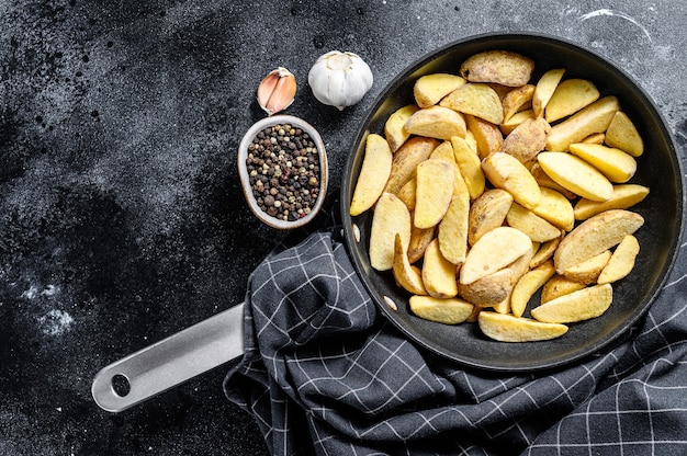 Bevroren aardappelpartjes in een pan. Franse frietjes. Zwarte achtergrond. Bovenaanzicht. Kopieer ruimte.