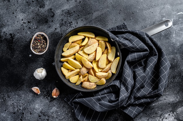 Bevroren aardappelwiggen in een pan. Franse frietjes. Zwarte achtergrond. Bovenaanzicht