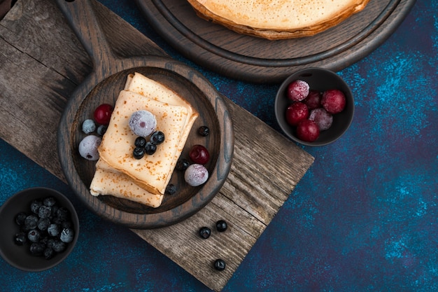 Bevroren bessen op gebakken pannenkoeken op een donkerblauwe achtergrond.