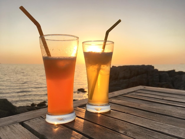 Bevroren cocktailglazen met rietjes op houten tafel over zee zonsondergang