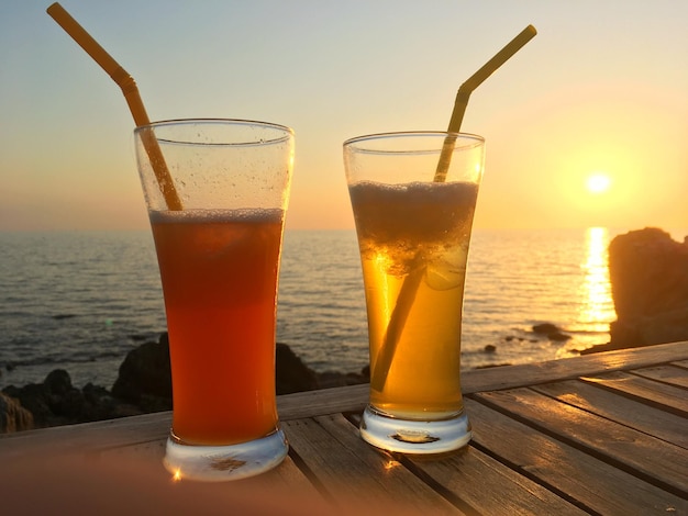 Bevroren cocktailglazen met rietjes op houten tafel over zee zonsondergang