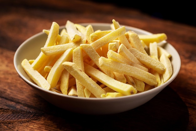 Bevroren frietjes op een bord op een houten achtergrond Halffabrikaat van bevroren aardappelen