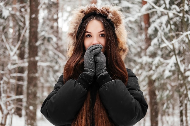 Foto bevroren jonge vrouw in jas en handschoenen die in het winterbos staan en handen buiten in het park opwarmen