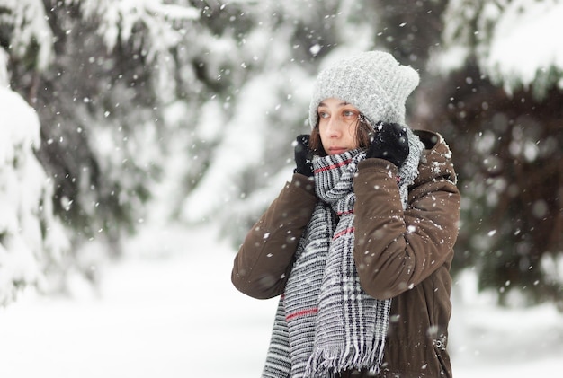 Bevroren jonge vrouw in warme kleren in besneeuwd winterweer in park of bos