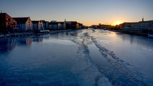 Foto bevroren rivier te midden van gebouwen tegen de hemel bij zonsondergang