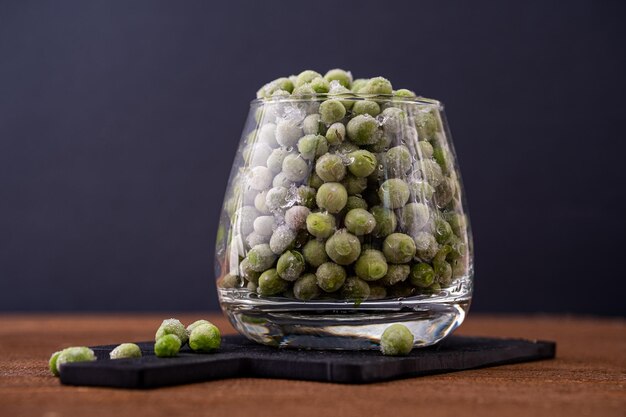 Bevroren verse groene erwten Groene erwten in een glazen transparante beker op een donkere achtergrond