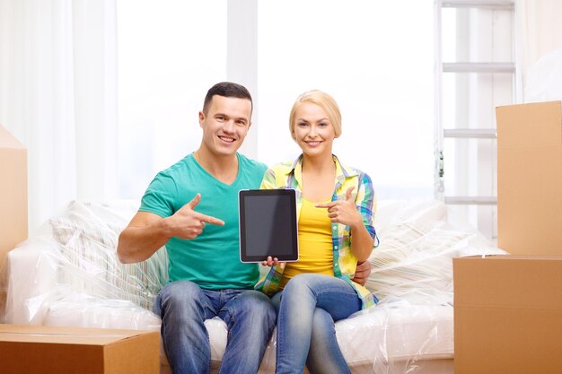 bewegen, huis, technologie en paar concept - glimlachend paar ontspannen op de bank en wijzende vinger naar tablet pc-computer in nieuw huis