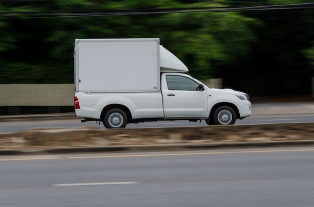 Foto bewegend beeld, kleine witte vrachtwagen die op de weg rijdt voor logistieke zaken.