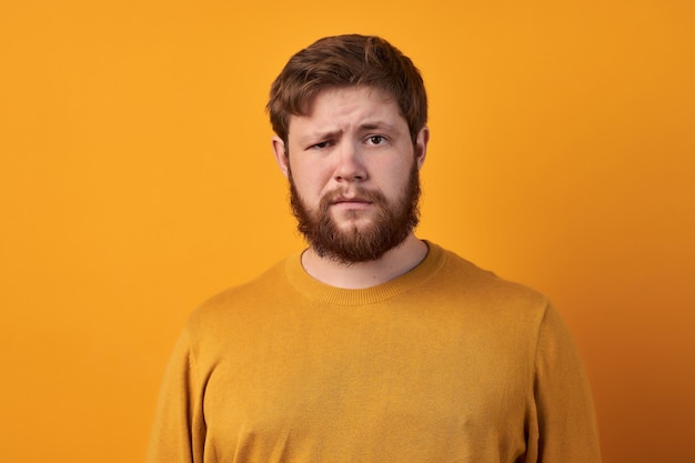 Bewildered man with thick ginger beard, raises eyebrows, reacts on fake news from friend, looks directly at camera