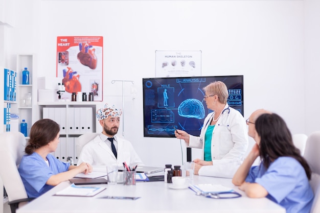 Bewustzijnsdokter die een headset draagt met sensoren voor hersengolven tijdens neurowetenschap, monitor toont moderne hersenstudie terwijl het team van wetenschappers het apparaat aanpast.