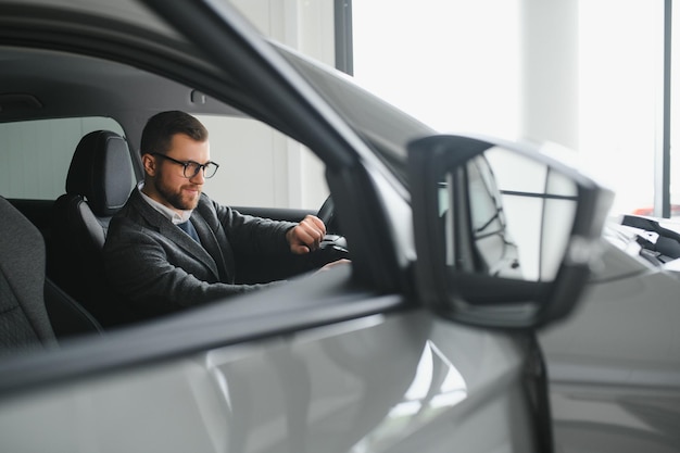 Bezoek aan autodealer Knappe bebaarde man streelt zijn nieuwe auto en glimlacht