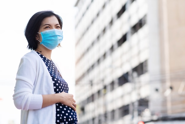 Bezorgd Aziatische zwangere vrouw in gezichtsmasker op buiten met nieuw normaal leven