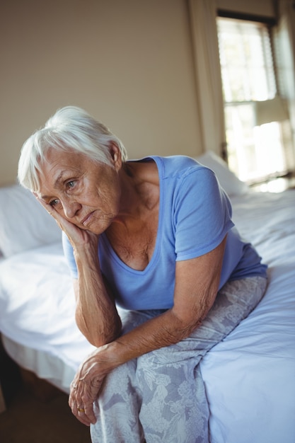 Bezorgd senior vrouw zittend op bed in de slaapkamer thuis