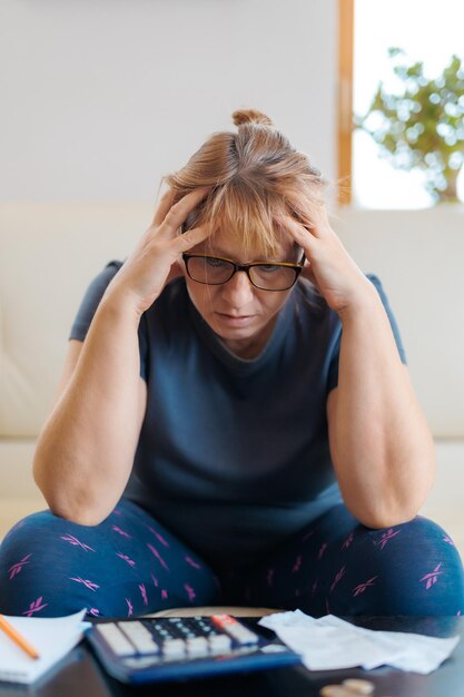 Foto bezorgde en wanhopige blanke vrouw die binnenlandse gelduitgaven berekent die papierwerk en bankrekeningen doet met een rekenmachine die lijdt aan stress bij financiële problemen en depressie