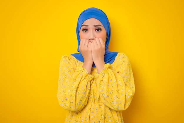 Bezorgde jonge Aziatische vrouw in casual kleding die nagels bijt, ziet er gestrest en nerveus uit geïsoleerd op gele achtergrond