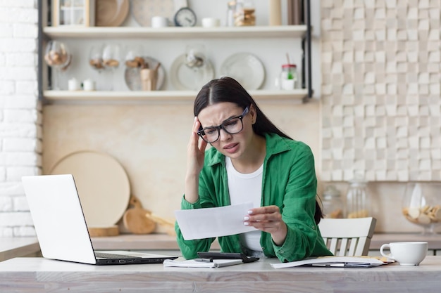 Bezorgde jonge vrouw die een ontvangen brief leest terwijl ze thuis in de keuken zit