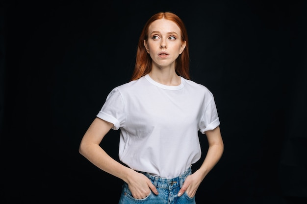 Bezorgde jonge vrouw intshirt en denim broek poseren met handen in de zakken op geïsoleerde achtergrond