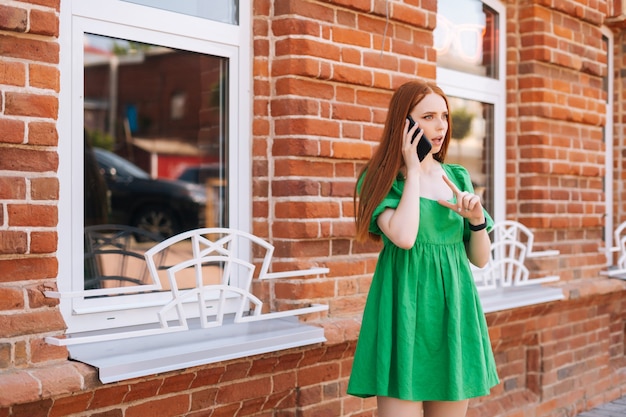 Bezorgde jonge vrouw praten op mobiele telefoon staande op straat in de zomerdag, onscherpe achtergrond, selectieve focus. Trieste ontevreden dame die buiten belt