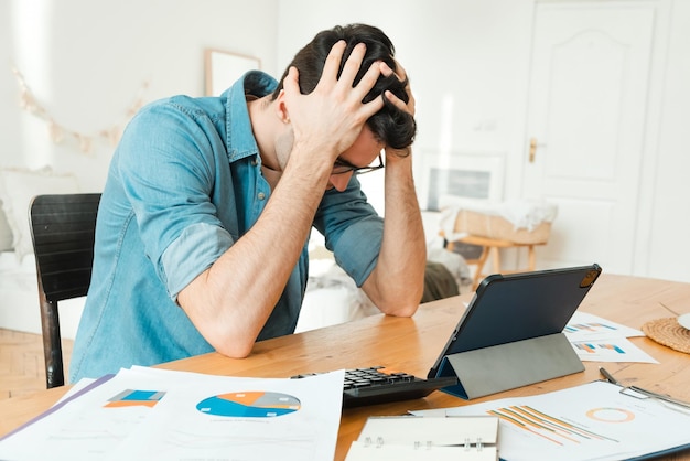 Bezorgde man die thuis aan tafel zit en zijn hoofd vasthoudt, bezorgd over zijn rekeningen Verlies van geld aan investeringen