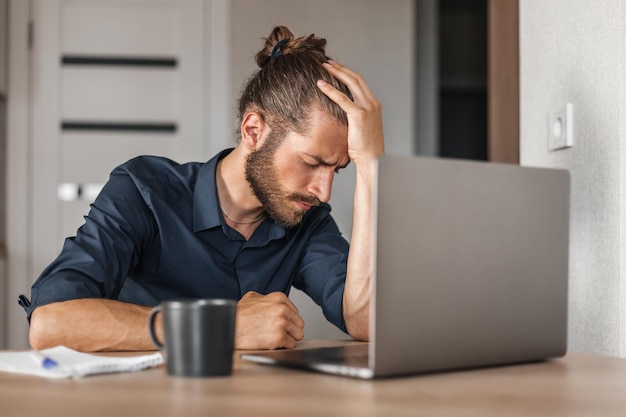 Bezorgde man zit aan werktafel met laptop