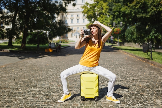 Bezorgde reiziger toeristische vrouw in hoed zittend op koffer nemen foto's op retro vintage fotocamera klampt zich vast aan het hoofd buiten. Meisje op weekendje weg naar het buitenland. Toeristische reis levensstijl.