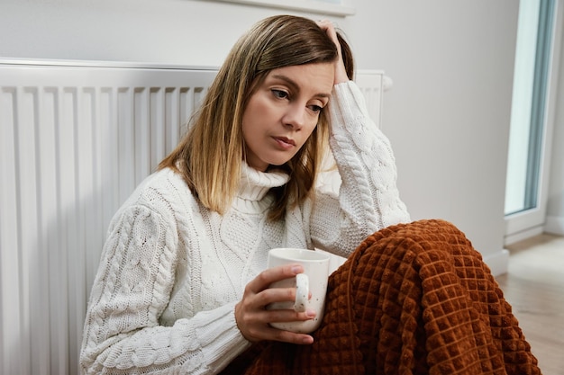 Foto bezorgde trieste vrouw zit onder deken in de buurt van verwarmingsradiator met kopje thee stijgende kosten in privé h