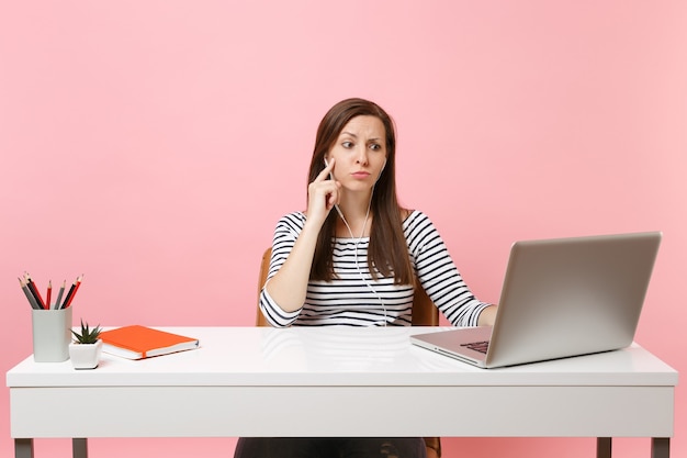 Bezorgde vrouw met oortelefoons die muziek luistert die videogesprek voert, zit en werkt op kantoor met een moderne pc-laptop