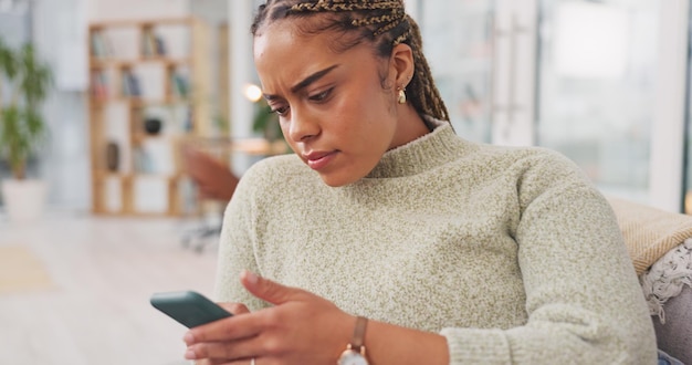 Bezorgde vrouw op de bank en smartphone met bezorgde uitdrukking die video's bekijkt in de woonkamer Afro-Amerikaanse vrouwelijke dame en mobiele telefoon met netwerksignaal sociale media of verbinding voor communicatie