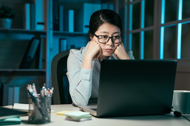 Bezorgde vrouwelijke zakenmensen die een laptopcomputer gebruiken terwijl ze in een donker modern kantoor zitten. peinzende aziatische japanse vrouw werknemer fronsen en kijken naar notebook pc-monitor in de late nacht brainstormen.