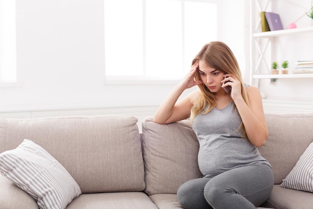 Bezorgde zwangere vrouw praten over de telefoon. triest aanstaande blondine die een serieus gesprek heeft met haar arts. gezondheidszorg, consultatie, zwangerschapsproblemen, bevallingsconcept