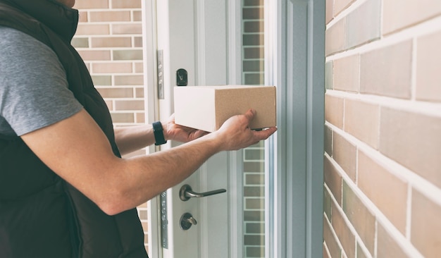 Bezorger geeft de kartonnen doos aan de klant aan de deur van zijn huis