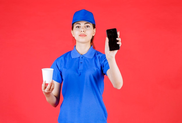 Bezorger in blauwe outfit met mobiele telefoon en kopje thee op rood.